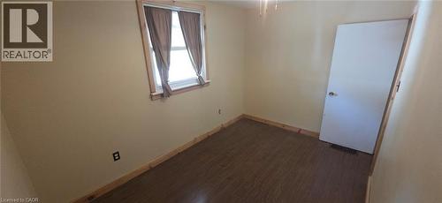 Room featuring wood-finish flooring, a double-hung window with natural wood trim, light beige wall paint, and a white interior door - 274 East 38Th Street, Hamilton, ON - Indoor Photo Showing Other Room