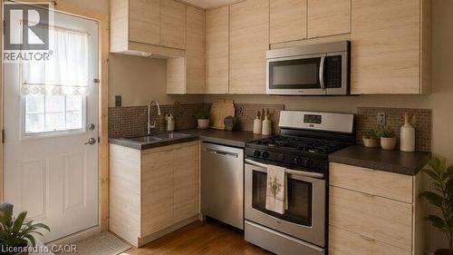 Modern kitchen featuring light wood-finish cabinetry, stainless steel appliances, dark countertops, and a mosaic tile backsplash - 274 East 38Th Street, Hamilton, ON - Indoor Photo Showing Kitchen With Double Sink