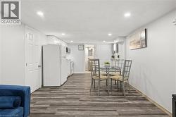 Open-concept living area featuring wood-finish flooring, recessed lighting, a white appliance kitchen, white cabinetry, and a dining area - 
