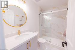 Bathroom featuring a frameless glass shower enclosure with white and gold veined wall tiles, a white vanity with a quartz countertop, a gold-framed circular mirror, and gold-finish fixtures - 