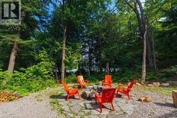 Outdoor fire pit area featuring a stone base, surrounded by gravel, and mature trees providing natural screening - 