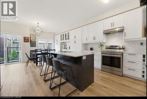 Kitchen featuring white upper and lower cabinetry, stainless steel appliances, a dark-toned island with seating, light wood-finish flooring, and a subway tile backsplash - 16 Raspberry Lane, Hamilton, ON - Indoor Photo Showing Kitchen With Upgraded Kitchen