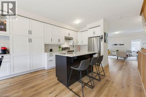 Kitchen featuring white shaker-style cabinetry, a dark-toned island with a light-toned countertop, stainless steel appliances, and light wood-finish flooring - 16 Raspberry Lane, Hamilton, ON - Indoor Photo Showing Kitchen With Upgraded Kitchen