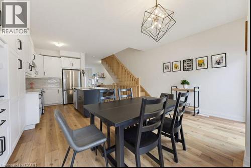 Open-concept living space featuring wood-finish flooring, a contemporary geometric chandelier, white cabinetry with black hardware, a tiled backsplash, and a wooden staircase - 16 Raspberry Lane, Hamilton, ON - Indoor Photo Showing Other Room
