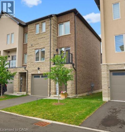 Modern townhouse exterior featuring a brick facade with stone accents, a single-car garage, and a small balcony with black railings - 16 Raspberry Lane, Hamilton, ON - Outdoor