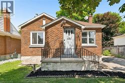 Brick-clad exterior with a prominent front entrance, featuring a concrete porch, black wrought iron railings, and a light gray front door - 