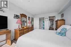 Bedroom featuring light-toned walls, wood-finish flooring, a built-in closet with shelving, and a visible doorway to a bathroom with a shower - 