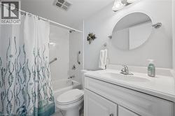 Bathroom featuring a white vanity with integrated sink, oval mirror, wall-mounted vanity lighting, a full-size bathtub with shower, and grab bars - 