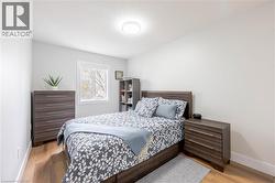 Bedroom featuring wood-finish flooring, white walls, and a window with white trim - 