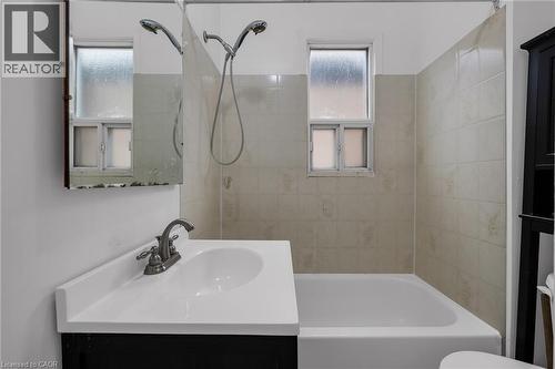 Bathroom featuring a white bathtub, a vanity with an integrated sink, a wall-mounted medicine cabinet, and a tiled shower surround - 29 Harrison Avenue, Hamilton, ON - Indoor Photo Showing Bathroom