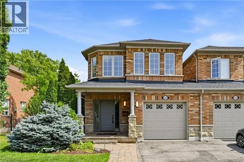 Brick facade residence featuring a covered front porch with white columns, a bay window on the second level, an integrated single-car garage, and a paver stone walkway - 5628 Stella Lane, Burlington, ON - Outdoor