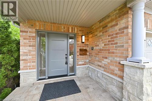 Covered front porch featuring a modern entry door with sidelights, brick facade, stone accents, exterior lighting, and a classical column - 5628 Stella Lane, Burlington, ON - Outdoor With Exterior