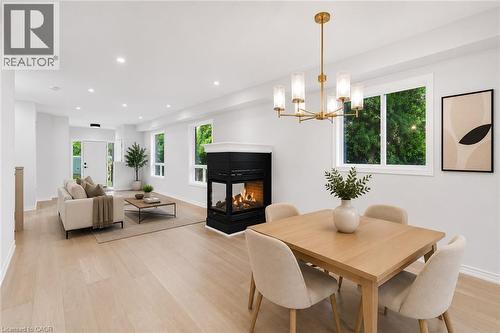 Open concept living and dining area featuring light wood-finish flooring, a contemporary central fireplace with a black surround, multiple windows, and recessed lighting - 5628 Stella Lane, Burlington, ON - Indoor Photo Showing Dining Room With Fireplace