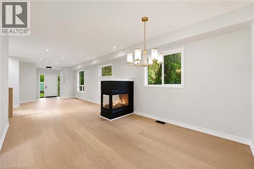 Open-concept living space featuring light wood-finish flooring, a modern gas fireplace with a black surround, recessed lighting, and a contemporary brass chandelier - 5628 Stella Lane, Burlington, ON - Indoor Photo Showing Other Room With Fireplace