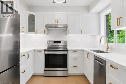U-shaped kitchen featuring white cabinetry with gold-finish hardware, stainless steel appliances, a single-basin sink with gold-finish faucet, and light wood-finish flooring - 5628 Stella Lane, Burlington, ON - Indoor Photo Showing Kitchen With Upgraded Kitchen