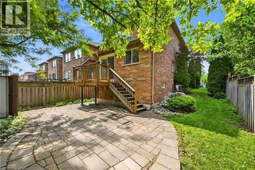 Rear exterior featuring a brick facade, a wooden deck with stairs to a paver patio, and a grass-lined perimeter - 5628 Stella Lane, Burlington, ON - Outdoor