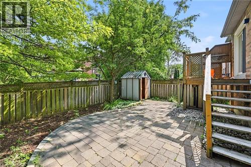 Expansive paver patio featuring a raised wood deck with lattice railing, a storage shed, and a full wooden privacy fence - 5628 Stella Lane, Burlington, ON - Outdoor