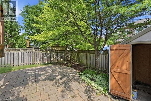 Paved patio area featuring interlocking pavers, a privacy fence, mature trees, and a utility shed with a wooden door - 5628 Stella Lane, Burlington, ON - Outdoor