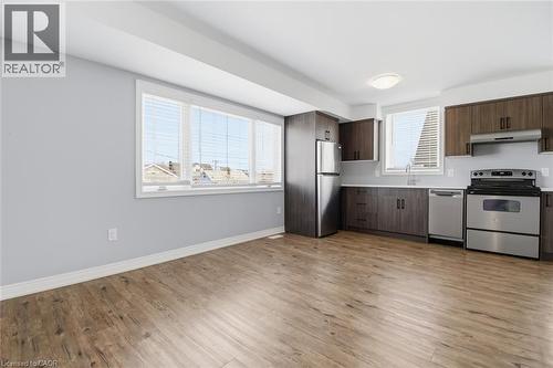 Open-concept kitchen featuring wood-finish flooring, dark wood cabinetry, stainless steel appliances, and light-toned countertops - 5 Hagar Street, Thorold, ON - Indoor Photo Showing Kitchen