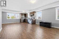 Open-concept living space featuring wood-finish flooring, a full kitchen with stainless steel appliances and dark wood cabinetry, and multiple windows with white blinds - 