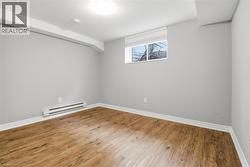Room with wood-finish flooring, light grey walls, white baseboards, and a window with white blinds - 