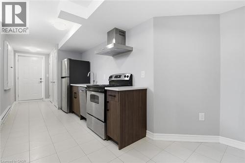 Compact kitchen area featuring stainless steel appliances, dark wood-finish cabinetry, light countertops, and square tile flooring - 5 Hagar Street, Thorold, ON - Indoor Photo Showing Kitchen