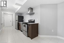 Compact kitchen area featuring stainless steel appliances, dark wood-finish cabinetry, light countertops, and square tile flooring - 