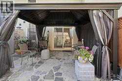 Flagstone patio featuring a dark metal gazebo with retractable privacy curtains, a fixed pergola roof, and a sliding glass door entry to the interior - 