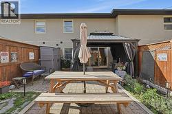 Paved backyard featuring a dark wood privacy fence, a built-in gazebo with drapes, and a sliding glass door entry to the main residence - 