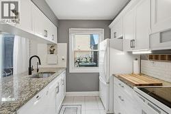 Galley kitchen featuring white cabinetry, granite-finish countertops, and a white subway tile backsplash - 