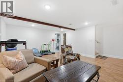 Finished lower level featuring recessed lighting, exposed wood ceiling beams, wood-finish flooring, and a stairway with a wood handrail - 