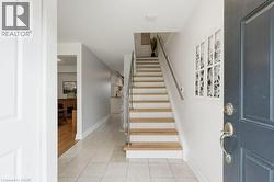 Entryway featuring light-toned tile flooring and a staircase with wood treads and a metal handrail - 