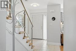 Entryway featuring a glass and stainless steel staircase railing, light wood-finish treads, a white paneled front door with sidelight, and light-toned tile flooring - 