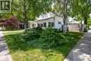 Front exterior featuring white siding, multiple windows with brown shutters, and a well-maintained lawn with mature trees and shrubbery - 5 Hawthorne Avenue, Simcoe, ON  - Outdoor 