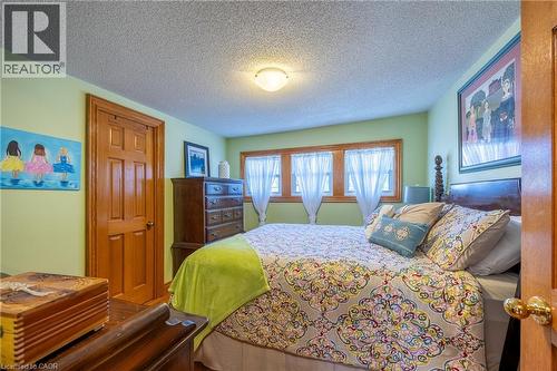 Bedroom featuring light green walls, a textured ceiling, a built-in flush mount light fixture, and natural wood trim around windows and doors - 5 Hawthorne Avenue, Simcoe, ON - Indoor Photo Showing Bedroom