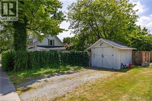 Detached white shed with barn-style doors and exterior lighting, gravel driveway, privacy hedge, and a partial view of the property's main structure - 5 Hawthorne Avenue, Simcoe, ON - Outdoor