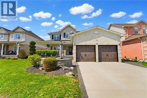 Brick facade residence featuring a two-car garage with wood-finish doors, a paved driveway, and mature landscaping - 29 Watson Crescent, Ayr, ON - Outdoor With Facade