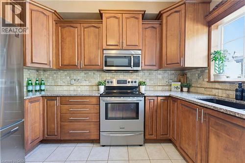 Kitchen featuring wood cabinetry, stainless steel appliances, granite countertops, tile backsplash, and a large window - 29 Watson Crescent, Ayr, ON - Indoor Photo Showing Kitchen