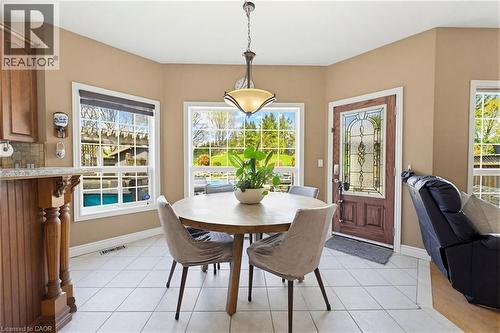 Tiled flooring throughout a bright dining area featuring multiple windows, a decorative entry door with leaded glass, and a built-in cabinetry section with a granite-look countertop and tile backsplas - 29 Watson Crescent, Ayr, ON - Indoor Photo Showing Dining Room