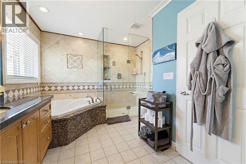 Bathroom featuring a corner soaking tub, a frameless glass shower enclosure, a dual-sink vanity with a dark countertop, and tiled walls and flooring - 29 Watson Crescent, Ayr, ON - Indoor Photo Showing Bathroom