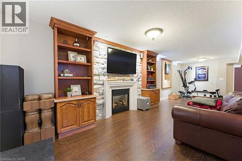 Entertainment space featuring wood-finish flooring, a stone-accented fireplace surround, and built-in wood shelving with lower cabinetry - 29 Watson Crescent, Ayr, ON - Indoor Photo Showing Living Room With Fireplace