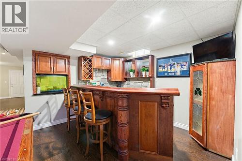 Custom built-in bar featuring carved wood details, a stone-finish backsplash, dark wood-finish flooring, recessed lighting, and a suspended ceiling - 29 Watson Crescent, Ayr, ON - Indoor