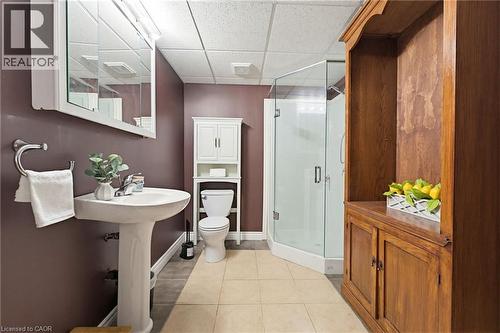 Bathroom featuring a pedestal sink, a frameless glass shower enclosure, a white toilet with an over-the-toilet storage cabinet, a mirrored medicine cabinet, and light-toned tile flooring - 29 Watson Crescent, Ayr, ON - Indoor