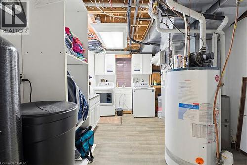 Utility space featuring exposed ceiling joists, wood-finish flooring, built-in shelving, a laundry area with upper and lower cabinetry, and visible water heater infrastructure - 29 Watson Crescent, Ayr, ON - Indoor Photo Showing Basement