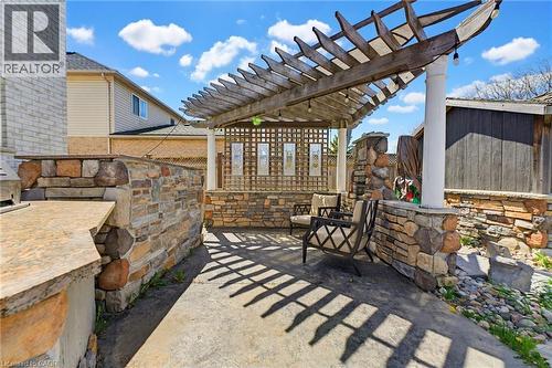Outdoor patio featuring a wooden pergola, stone-clad retaining walls, a built-in stone counter, and a paved surface - 29 Watson Crescent, Ayr, ON - Outdoor With Deck Patio Veranda