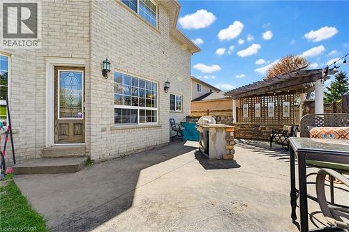 Expansive concrete patio with a built-in outdoor kitchen, pergola structure, and a stone accent wall - 29 Watson Crescent, Ayr, ON - Outdoor