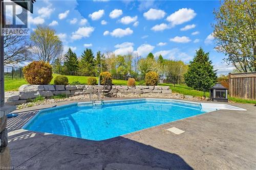 In-ground swimming pool with stamped concrete surround, stone retaining wall, and verdant landscaping - 29 Watson Crescent, Ayr, ON - Outdoor With In Ground Pool With Backyard