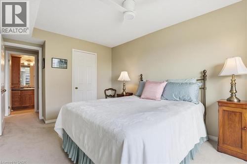 Carpeted bedroom featuring a ceiling fan, a brass bed frame, a paneled door, and a doorway to a bathroom with wood-finish cabinetry - 10 Ellen Street E Unit# 808, Kitchener, ON - Indoor Photo Showing Bedroom