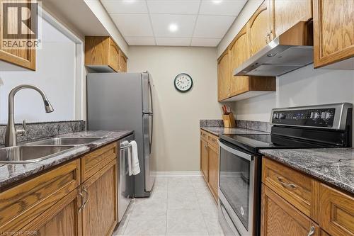 Galley kitchen featuring wood cabinetry, stone countertops, stainless steel appliances, a double basin sink, and recessed lighting - 10 Ellen Street E Unit# 808, Kitchener, ON - Indoor Photo Showing Kitchen With Double Sink
