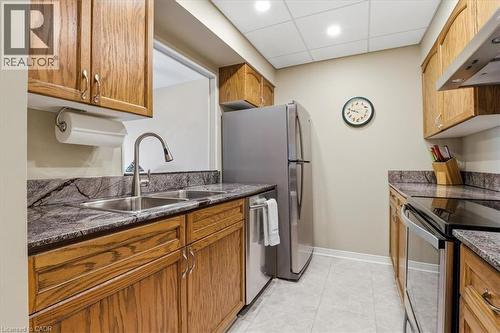 Kitchen featuring wood cabinetry, stainless steel appliances, a double basin sink, stone countertops with matching backsplash, and recessed lighting - 10 Ellen Street E Unit# 808, Kitchener, ON - Indoor Photo Showing Kitchen With Double Sink